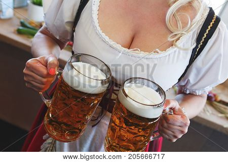 Girl in a traditional dress with a big breasts and deep neckline holds full mugs of beer during the celebration of the Oktoberfest