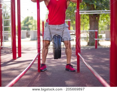 A strong man with sexy body is doing exercises on his feet. A handsome young man lifts weights with his feet in the park.