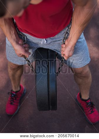 A strong man with sexy body is doing exercises on his feet. A handsome young man lifts weights with his feet in the park.
