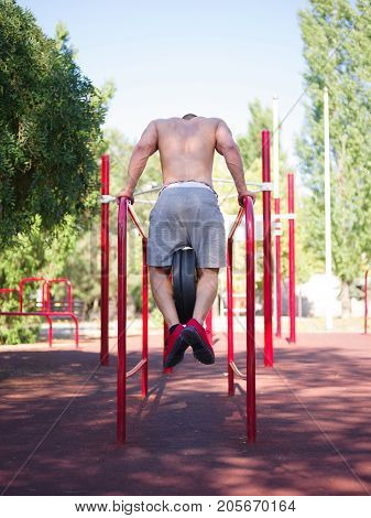 A strong man with sexy body is doing exercises on his feet. A handsome young man lifts weights with his feet in the park.