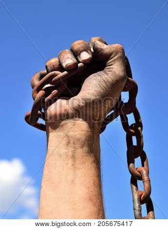man's hand wrapped in an iron rusty chain lifted up against a blue sky