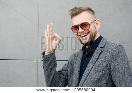 smiling man with a beard in sunglasses and jacket showing ok