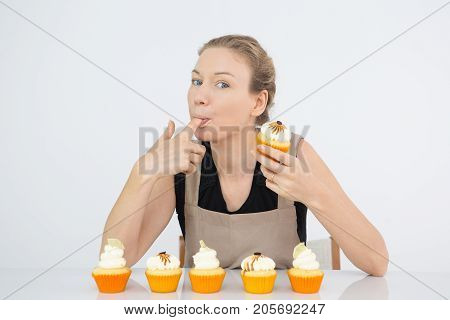 Funny woman licking finger with buttercream and looking at camera. Attractive confectioner tasting icing for cupcakes. Mouthwatering concept