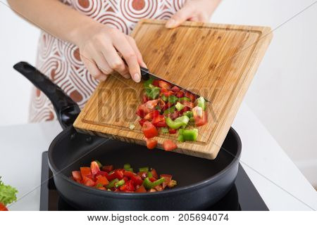 Unrecognizable woman cooking vegetable stew and adding fresh vegetables in pan on hotplate. Close-up of housewife cooking dinner. Recipe concept