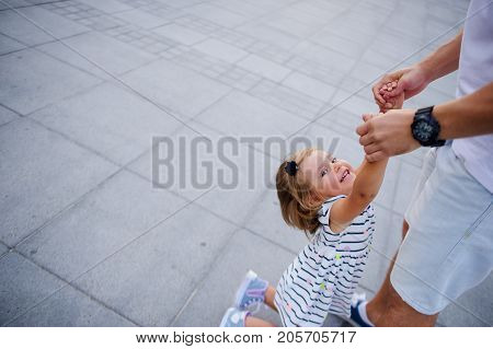 Young dad is playing with a charming little daughter. The man is holding the baby by the handles.. The child rejoices.