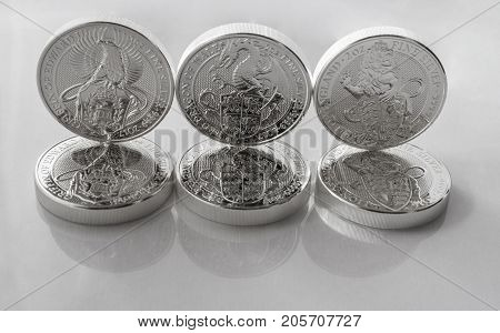 On a gray background are silver coins of an investment silver from a British mints. Dragon of Wales Lion of England and Griffin of Edward III.