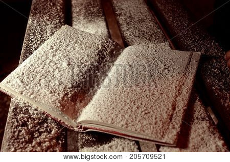 The opened snowbound book on the banch in the winter night park