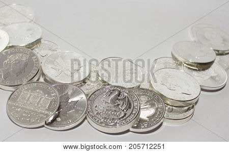 On a gray background are silver coins of an investment silver from an Austrian Canadian and British mints. Vienna Philharmonic Orchestra and Maple Leaf and Dragon of Wales.