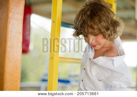 Mischievous boy 10-11 years old on the playground. The boy holds his hand to the crossbar of the Swedish wall. He has a cheerful and reckless look.