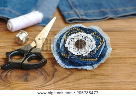 Handmade denim flower jewellery. Scissors, thread, thimble, needle, female old jeans on a wood background. Sewing projects to recycle old jeans. Closeup