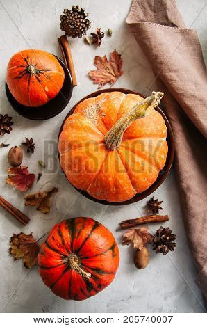 Three pumpkins maple leaves pecans and spices over white stone baclground. Autumn season Thanksgiving concept.