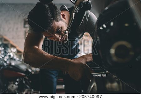 young handsome professional automechanic repairing motorbike in workshop