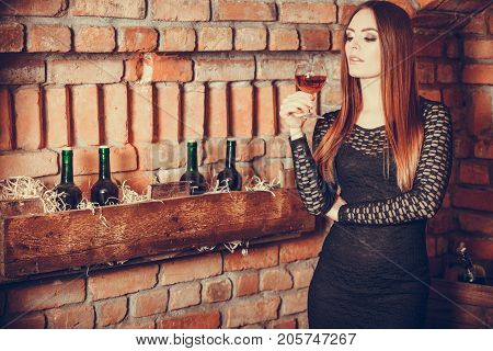 Elegant beauty lady long hair full make up wearing black dress tasting wine in rural cottage interior celler