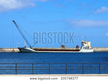 Emprty container ship in a harbour prior to loading with crane on the dock and blue sky and railings