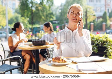 Mood-boosting conversation. Beautiful young woman talking on the phone and smiling while drinking coffee on the terrace of a restaurant