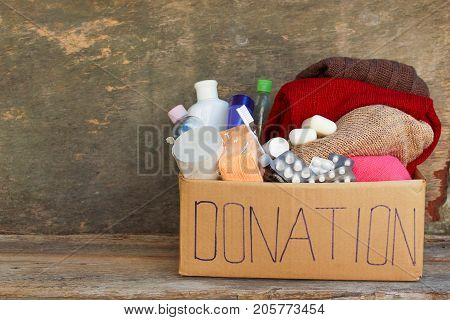 Donation box with clothes, living essentials on wooden background