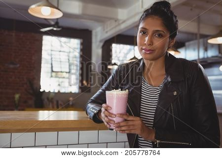 Portrait of youngwoman holding milkshake glass at counter in cafe