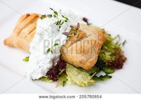 Traditional russian pie - coulibiac. Baked puff pastry filled with smoked salmon, served with sour cream sauce
