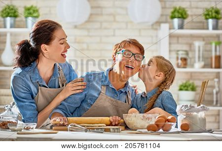 Happy loving family are preparing bakery together. Granny, mom and child daughter girl are cooking cookies and having fun in the kitchen. Homemade food and little helper.