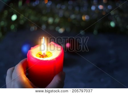 Burning Red Candle In A Hand On Christmas Decoration Background.