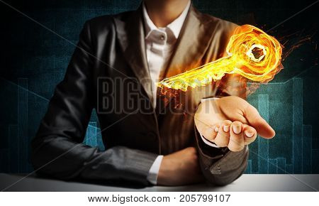 Closeup of businessman in black suit keeping flaming key symbol in hand with dark background.
