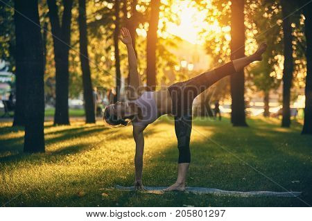 Beautiful sporty fit yogini woman practices yoga asana Ardha Chandrasana - Half Moon pose in the park at sunset