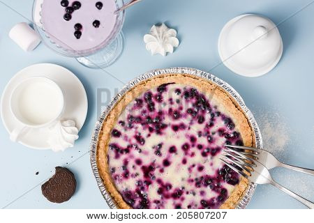 Homemade blueberry pie with cream filling served with blueberry smoothie marshmellow cookie and milk on pale blue table above view
