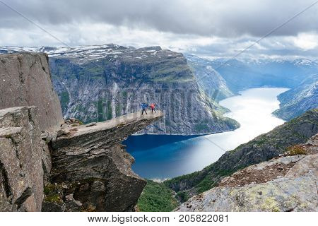 Trolltunga is a tourist attraction of Norway. Amazing place with a view of the lake and mountains. Couple of tourists is standing on a rock