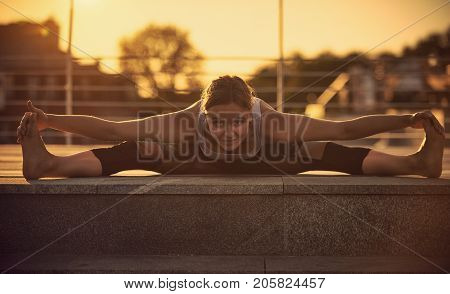 Young attractive woman practicing yoga, sitting in Samakonasana Straight angle posture in the terrace at sunset
