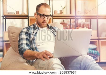 What a difficult task. Totally absorbed in work thoughtful millennial guy sitting with a laptop on his knees and working on a serious business project.