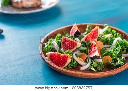 Autumn salad of arugula, figs in a brown earthenware plate on a dark background.