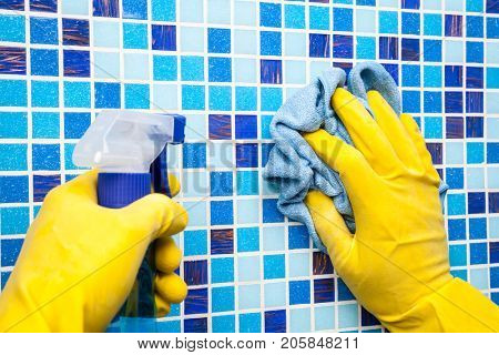 Person doing chores in bathroom at home cleaning tiled wall with sprayer and microfiber towel