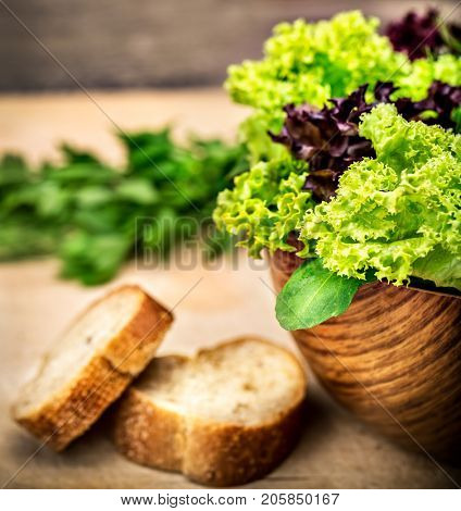 Fresh green salad in the wooden bowl with two piece of tasty bread on the table, organic nutrition, healthy delicious food, vegetarian diet