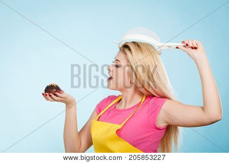 Baking tasty desserts sweets at home concept. Woman holding delicious sweet chocolate cupcake wearing apron and colander on head as hat.
