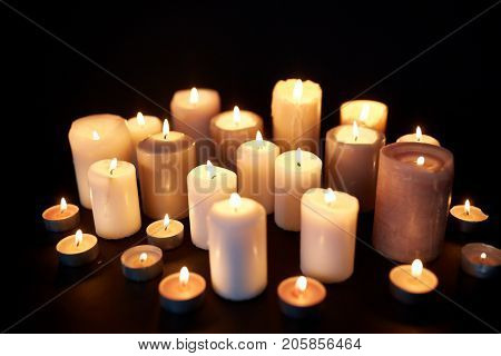 mourning and commemoration concept - candles burning in darkness over black background