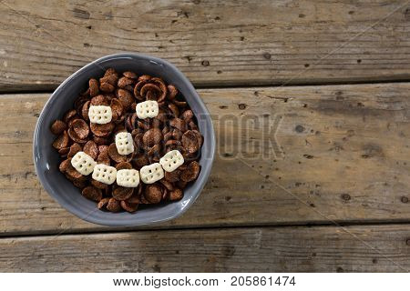 Chocolate cornflakes with honeycomb cereal forming smiley face in bowl on wooden table