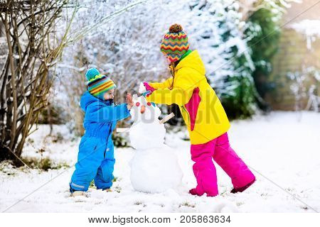 Children build snowman. Kids building snow man playing outdoors on sunny snowy winter day. Outdoor family fun on Christmas vacation. Boy and girl play snow balls. Winter clothing for baby and toddler.