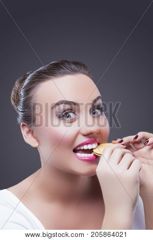 Food Concepts. Portrait of Surprised Caucasian Brunette Female Biting Round Cookie. Demonstrating Surprised Facial Expression.Against Gray.Vertical Image