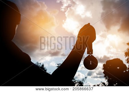 Blurred of silhouette busunesswoman hands raised and holding gold medals with ribbon against sunset background to show team success in business Winners success award concept.