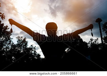 Blurred of silhouette businesswoman hands raised and holding gold medals with ribbon against sunset background to show team success in business Winners success award concept.