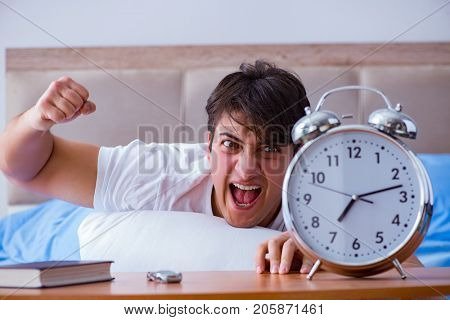 Man in bed frustrated suffering from insomnia with an alarm cloc