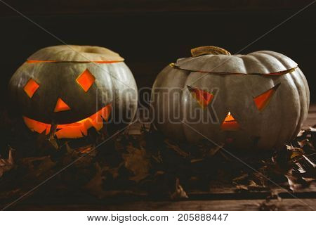 Close up of illuminated kack o lanterns with autumn leaves arranged on table