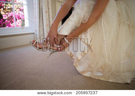 Low section of bride in weding dress wearing sandals at home