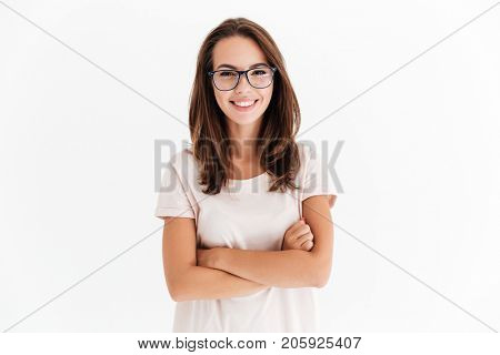 Joyful brunette woman in eyeglasses posing with crossed arms and looking at the camera over white background