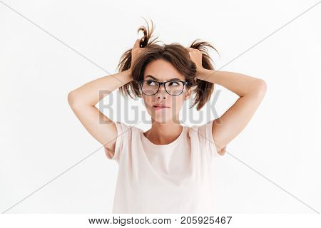 Thoughtful brunette woman in eyeglasses holding hair and looking away over white background