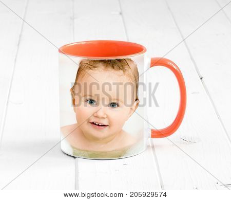 Small orange cup with bright orange handle and a printed face of a baby