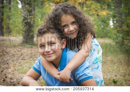 In the autumn forest a small curly sister lovingly embraces her older brother lovingly.