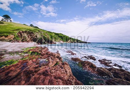 Red rocks and foamy blue sea on a sunny summer´s day at Talland Bay in South Cornwall, England.