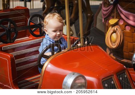 little boy is riding on the attractions in park, happy child looks at car at attractions
