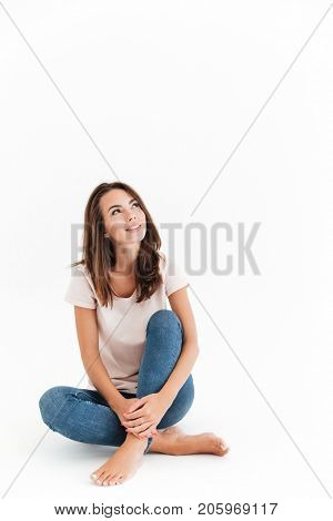 Vertical image of happy brunette woman sitting on the floor and looking up over white background